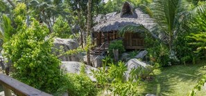 A rustic hut with a thatched roof surrounded by lush greenery and rocks.