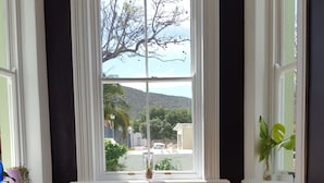 Una mesa de comedor dispuesta con varios platos, una ventana con vistas a un árbol y una colina, y una planta en el alféizar.