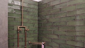 Ducha con pared de ladrillo verde, cabezal de ducha de mano y toallero con una toalla rosa.