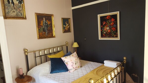 A bedroom with a bed, pillows, a bedside table, a lamp, and framed artwork on the wall. - Montagu Manor (Montagu)