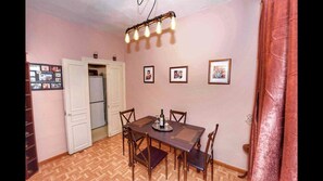 Uma sala de jantar com mesa e cadeiras de madeira, um candelabro e quadros nas paredes.