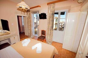 Quarto de hotel com cama, uma cadeira, televisão e varanda com cortinas.