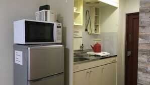 Een kleine keuken met een roestvrijstalen koelkast, een witte magnetron en een rode waterkoker op het aanrecht.