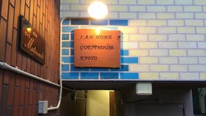 Een bord met de tekst 'I AM HOME GUESTHOUSE KYOTO' bevestigd aan een muur met een bakstenen patroon.