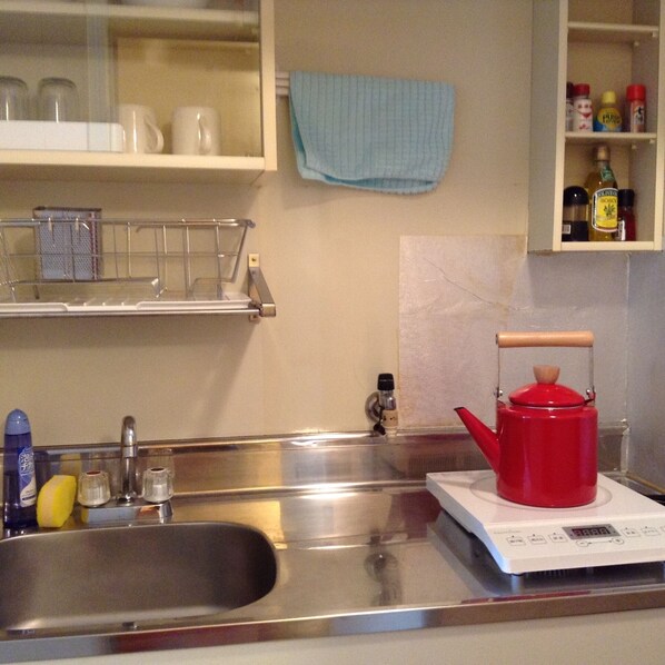 Una cocina con un lavamanos de acero inoxidable, una tetera roja sobre una balanza digital y varios utensilios de cocina sobre la encimera.