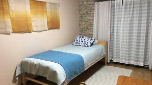 Un dormitorio pequeño y ordenado con una cama individual, una silla de madera, una mesa y una ventana con cortinas.