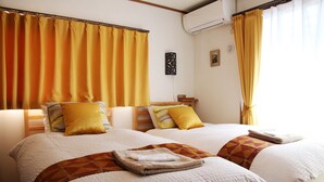 Een hotelkamer met twee bedden, elk voorzien van een witte dekbedovertrek en een bruine geometrische plaid. Er is een houten hoofdbord, een wandairconditioning en een klein decoratief object aan de muur.