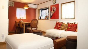 Een kamer met een bed, een slaapbank, een eettafel met stoelen, een ventilator en een klok aan de muur.