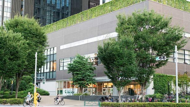 Een modern gebouw met een groen dak, grote ramen en een zebrapad met fietsers.