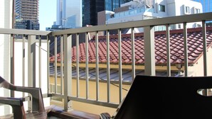 Een balkon met uitzicht op een stadslandschap, inclusief hoge gebouwen en een gebouw met een rood dak.