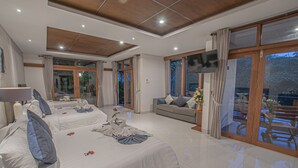 Amplia habitación de hotel con dos camas, un sofá, un televisor y ventanas amplias con vistas al exterior.
