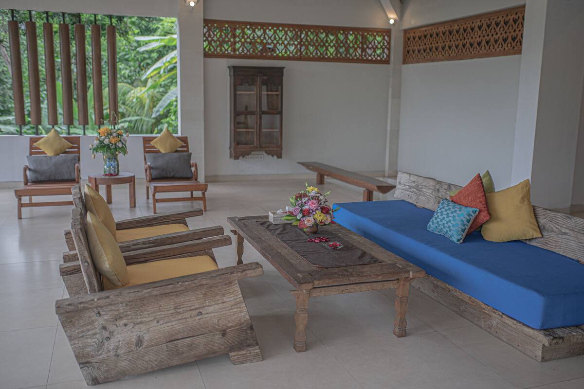 A room with a wooden sofa, two armchairs, a coffee table, and a window with a view of greenery.