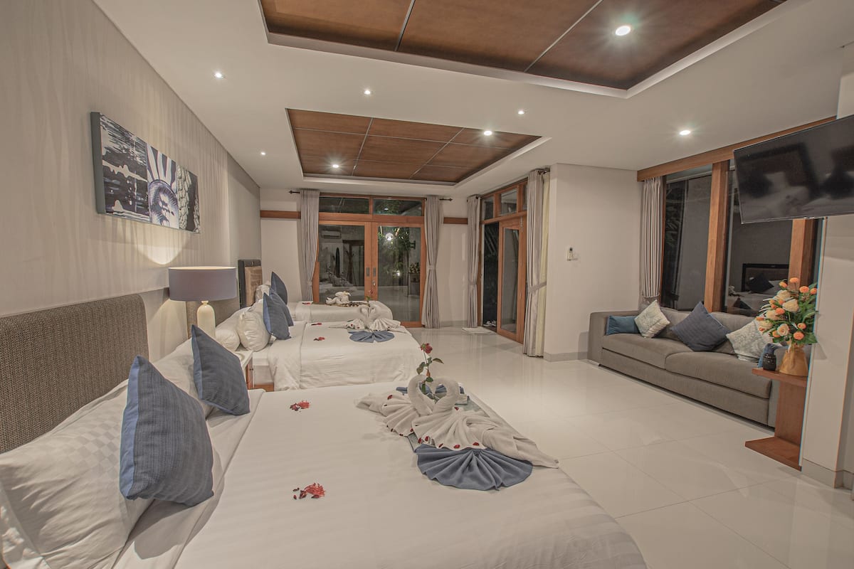 A hotel room with two beds, a sofa, a TV, and a large window.