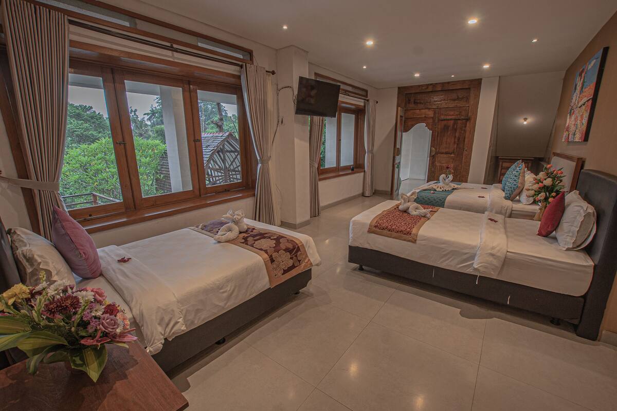 A hotel room with two beds, a TV, a large window, and a view of greenery outside.