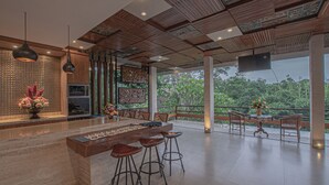 Un área de bar amplia con techo de madera, un ventanal con vistas a la vegetación y una barra moderna con taburetes.