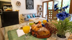 Ein Frühstückstisch mit Croissants, Brot, Obst und Saft, im Hintergrund ein Buddha-Gemälde und ein Bücherregal.