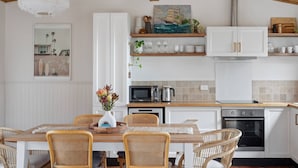 Een moderne keuken met witte kasten, een eethoek met rieten stoelen en een hanglamp.