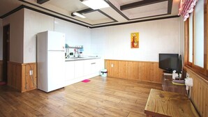 Cocina compacta con refrigerador, pileta y muebles de madera. Hay un televisor sobre un atril de madera y una mesita.