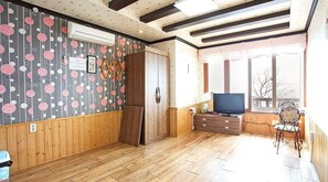 A room with wooden walls and floors, a large wardrobe, a television, and a window with a view of trees.
