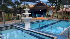 A swimming pool with a central fountain, surrounded by lounge chairs and a covered seating area. - Rufina's Leisure Center (Tagum)