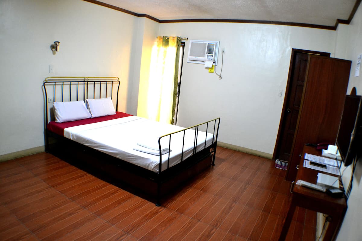 Une chambre à coucher avec un lit en métal, un plancher en bois, une couvre-lit rouge et une armoire en bois.