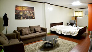 A hotel room with a bed, a sofa, a small table, and a cityscape painting on the wall. - Rufina's Leisure Center (Tagum)