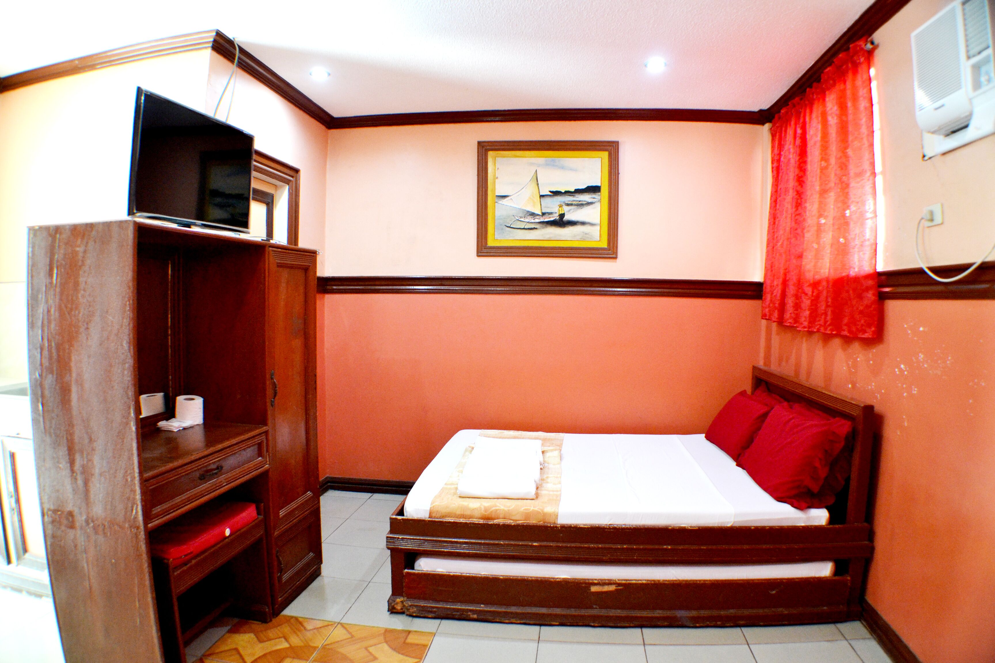 A bedroom with a wooden bed, a television on a stand, a painting on the wall, and a red curtain.