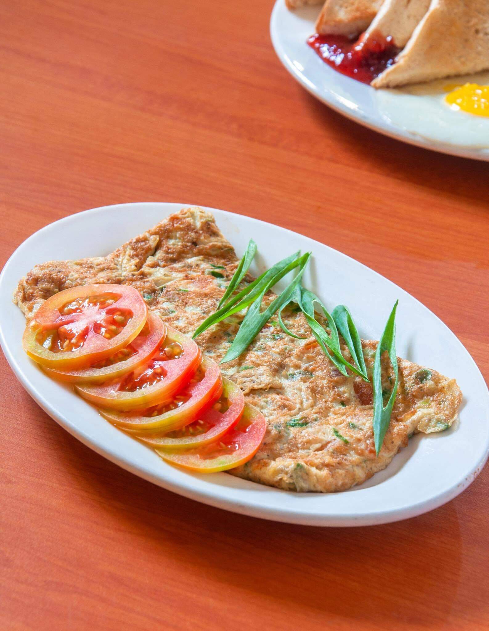 A plate of food with a slice of tomato and green garnish on an oval plate.