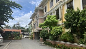 A street view with a two-story building featuring a balcony with lush greenery and a flower bed with red flowers. - Rufina's Leisure Center (Tagum)
