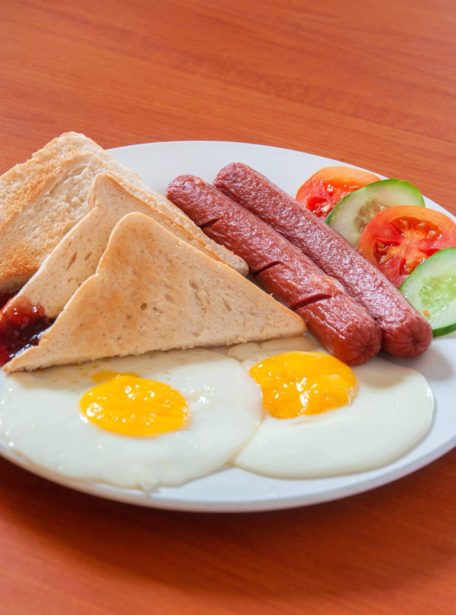 Un plato con tostadas, salchichas, huevos, tomates y pepinos en rodajas.