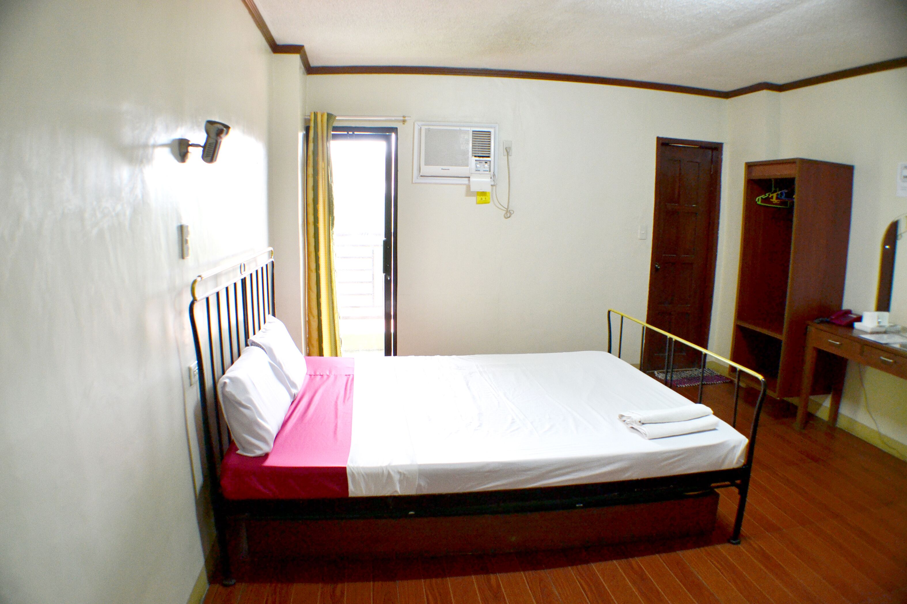 A single bed with a wooden frame, a radiator, a wardrobe, and a desk with a chair in a room with wooden flooring and white walls.