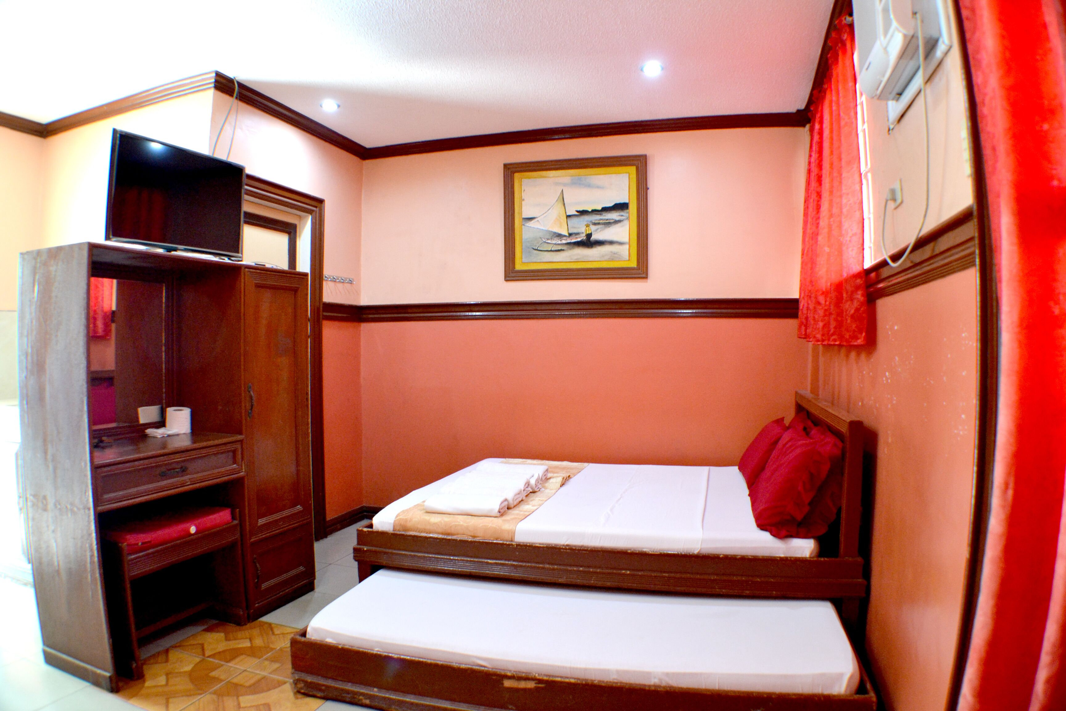 A hotel room with a bed, a desk with a television, and a painting on the wall.