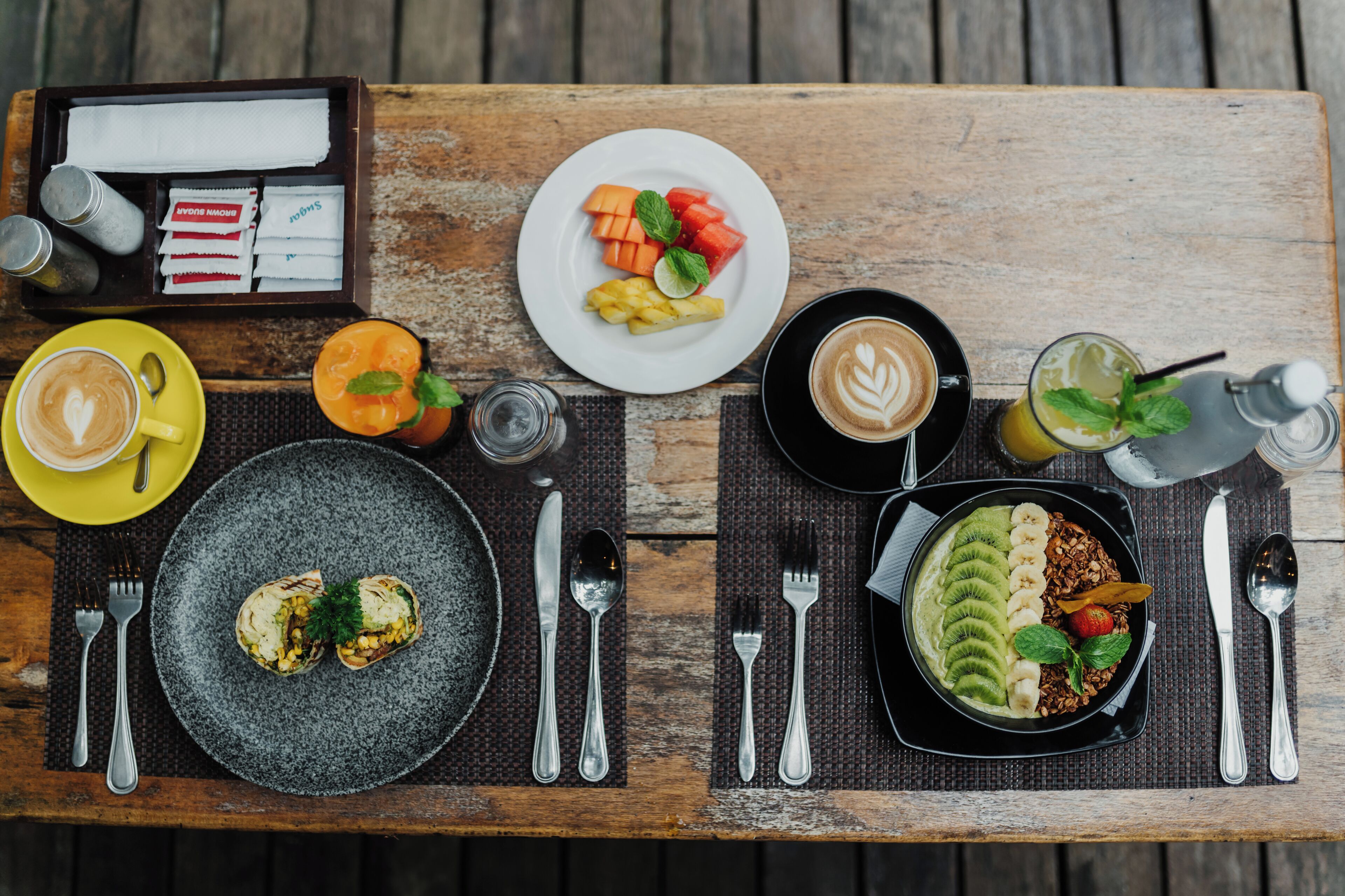 Mesa de madeira com itens de café da manhã, incluindo café, frutas e uma tigela de granola.