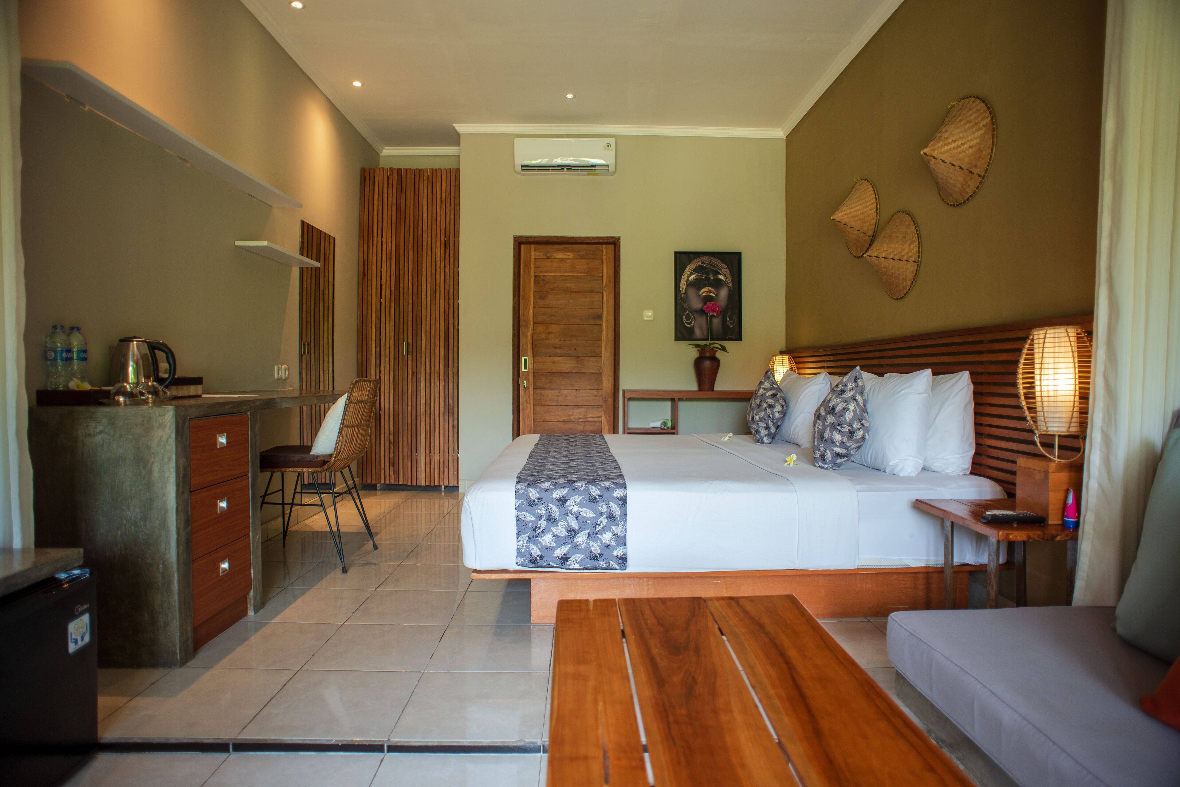 Habitación de hotel con cama, sofá, escritorio con silla, kitchenette pequeña y baño.