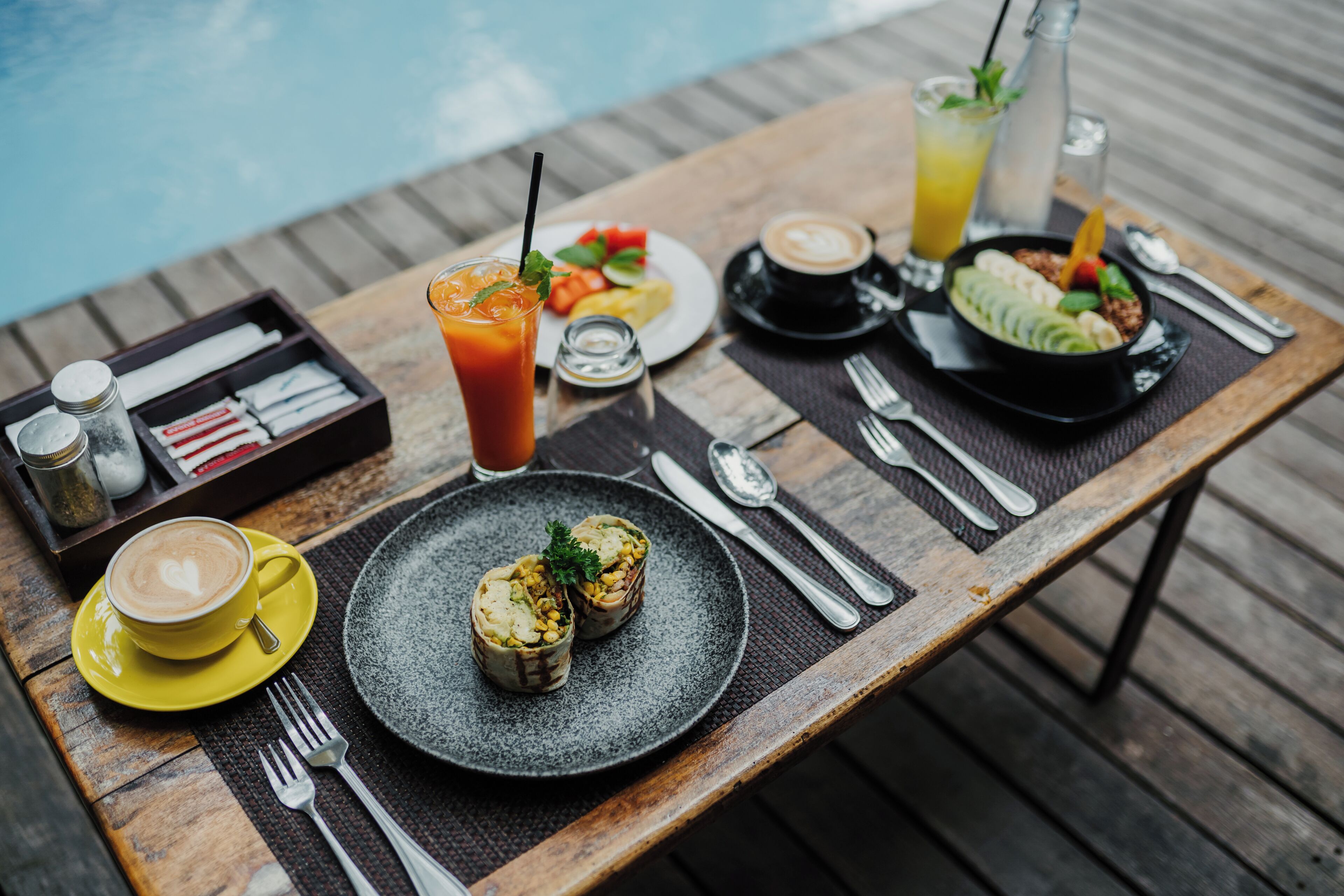 A wooden table with a variety of breakfast items including a plate of eggs, a cup of coffee, and a glass of orange juice.
