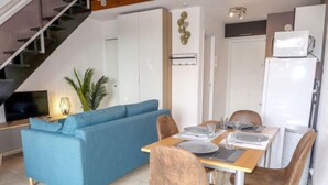 Una sala de estar moderna con un sofá azul, una mesa de comedor preparada para cuatro comensales y una escalera que conduce a un nivel superior.