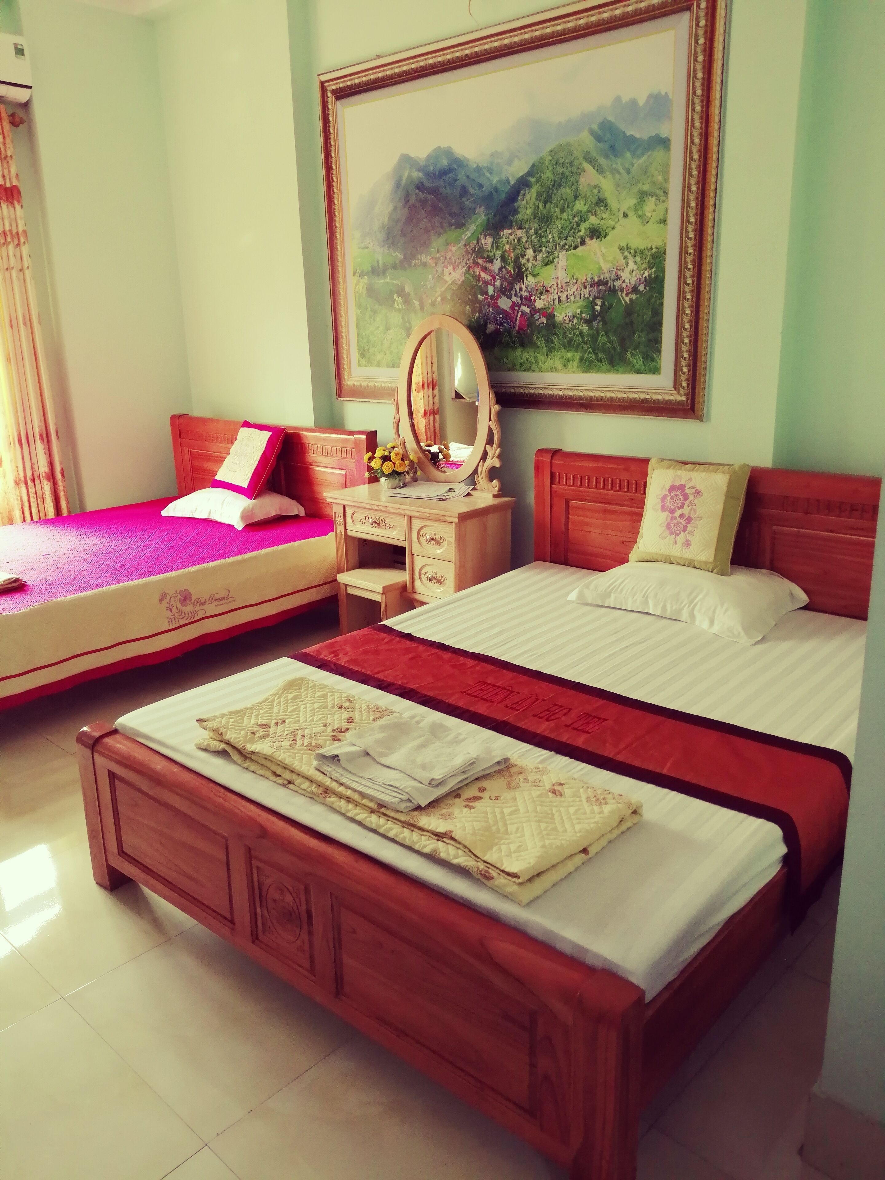 A hotel room with two beds, a wooden dresser, a mirror, and a painting on the wall.