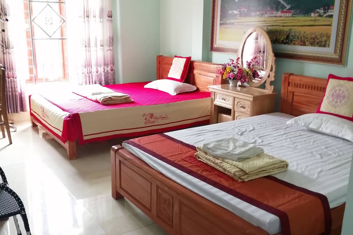 Une chambre d’hôtel avec deux lits, une tête de lit en bois, une table de chevet avec un miroir, une fenêtre avec des rideaux et un tableau au mur.