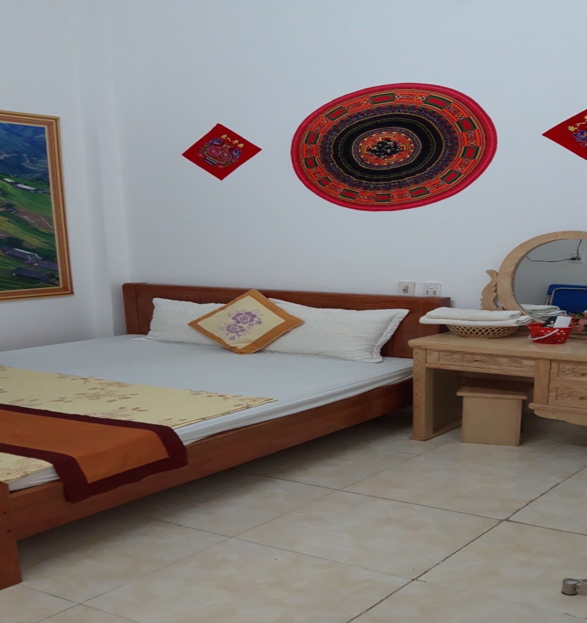 A bedroom with a bed, a wooden dresser, a mirror, and a wall hanging.