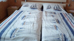 Una cama doble con una colcha a rayas y dos almohadas con diseño de veleros.