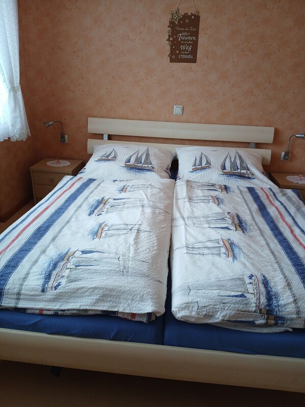A double bed with a striped bedspread and two pillows with sailboat designs.