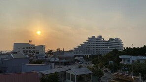 A modern building with multiple floors and a flat roof, surrounded by smaller structures and trees.