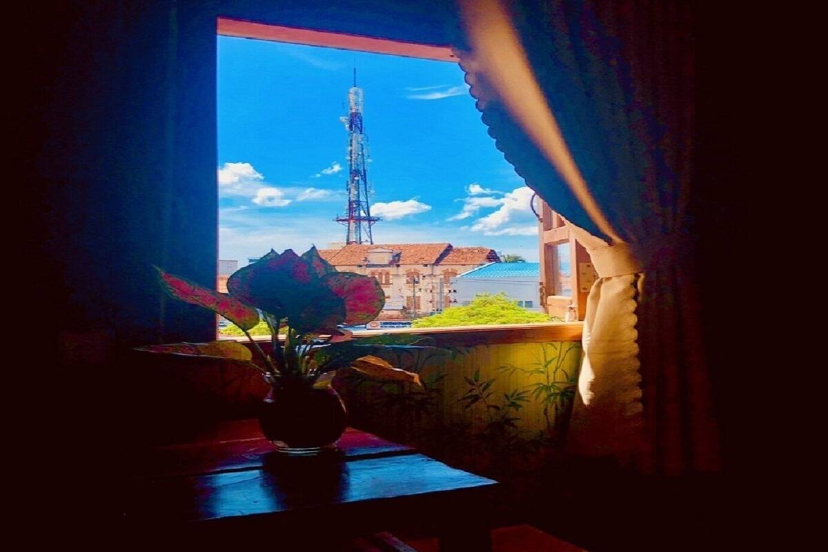 Een kamer met een raam dat uitkijkt op een gebouw met een hoge zendmast.