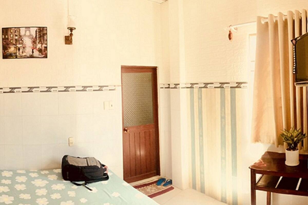 Hotelkamer met een bed, een bureau met een plant, een radiator, een deur en een foto aan de muur.