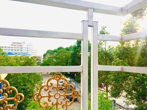 A balcony with a metal railing and decorative elements, overlooking a street with trees and buildings.