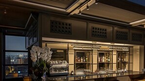 A bar area with a long counter, bar stools, and a view of the cityscape through large windows. - Azzap Hotel Galata (Istanbul)