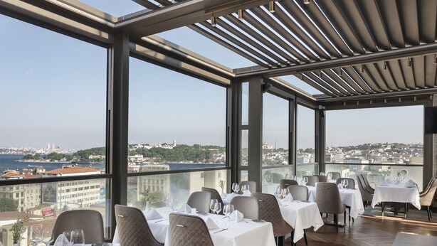 A restaurant with tables set for dining, large windows offering a city view, and a modern interior design. - Azzap Hotel Galata (Istanbul)