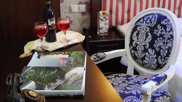 Um quarto com uma mesa de madeira, uma cadeira com almofada estampada, uma garrafa de vinho, duas taças de vinho e um livro de capa com paisagem.