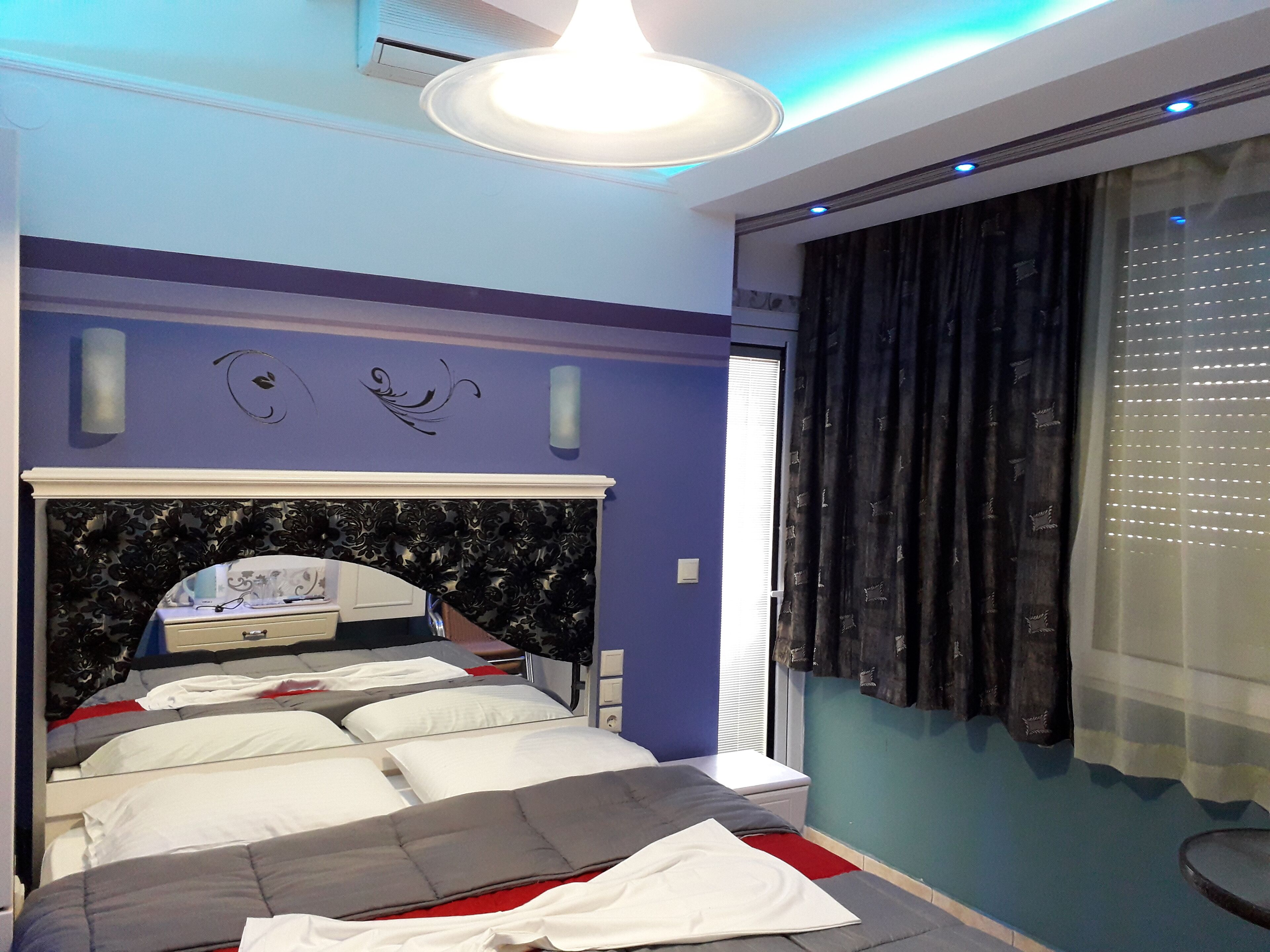 A bedroom with a bed, a headboard, a window with curtains, and a wall with decorative elements.
