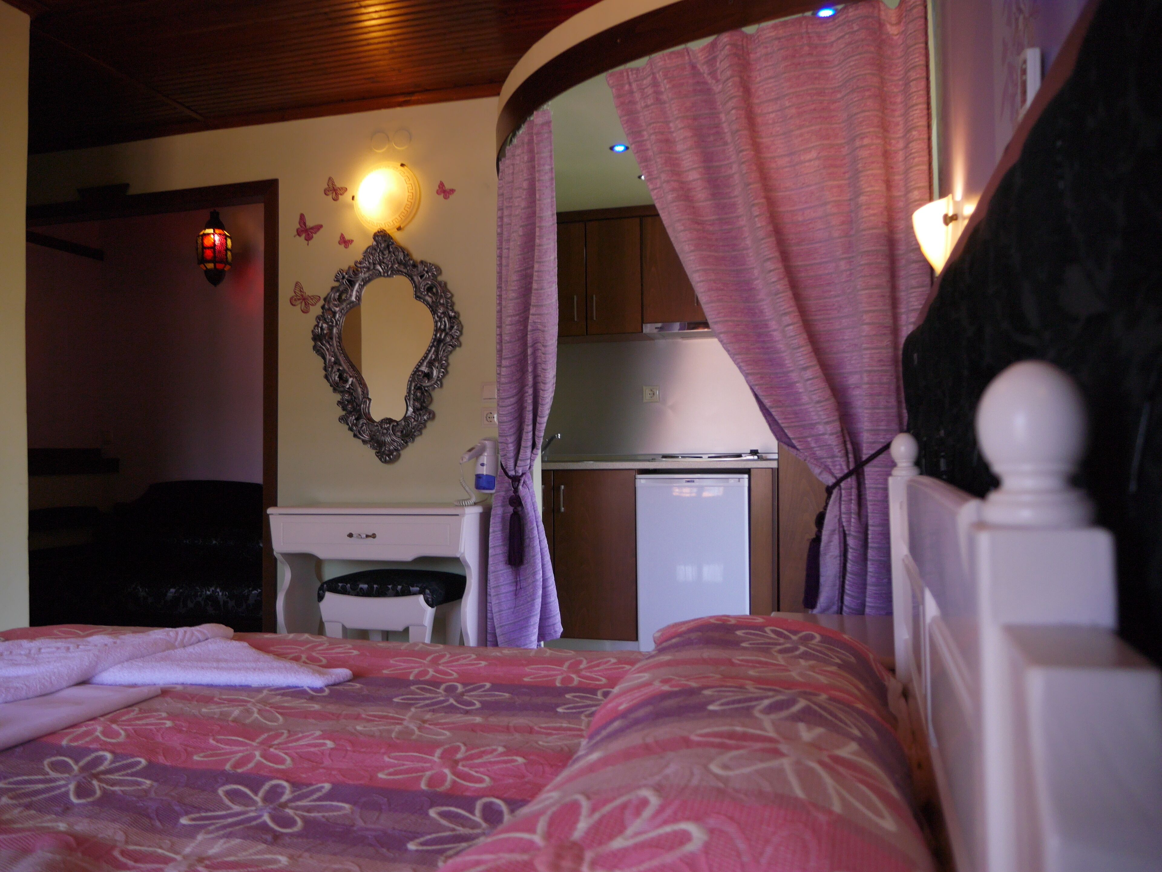 A bedroom with a bed, a dresser, a mirror, and a kitchenette.